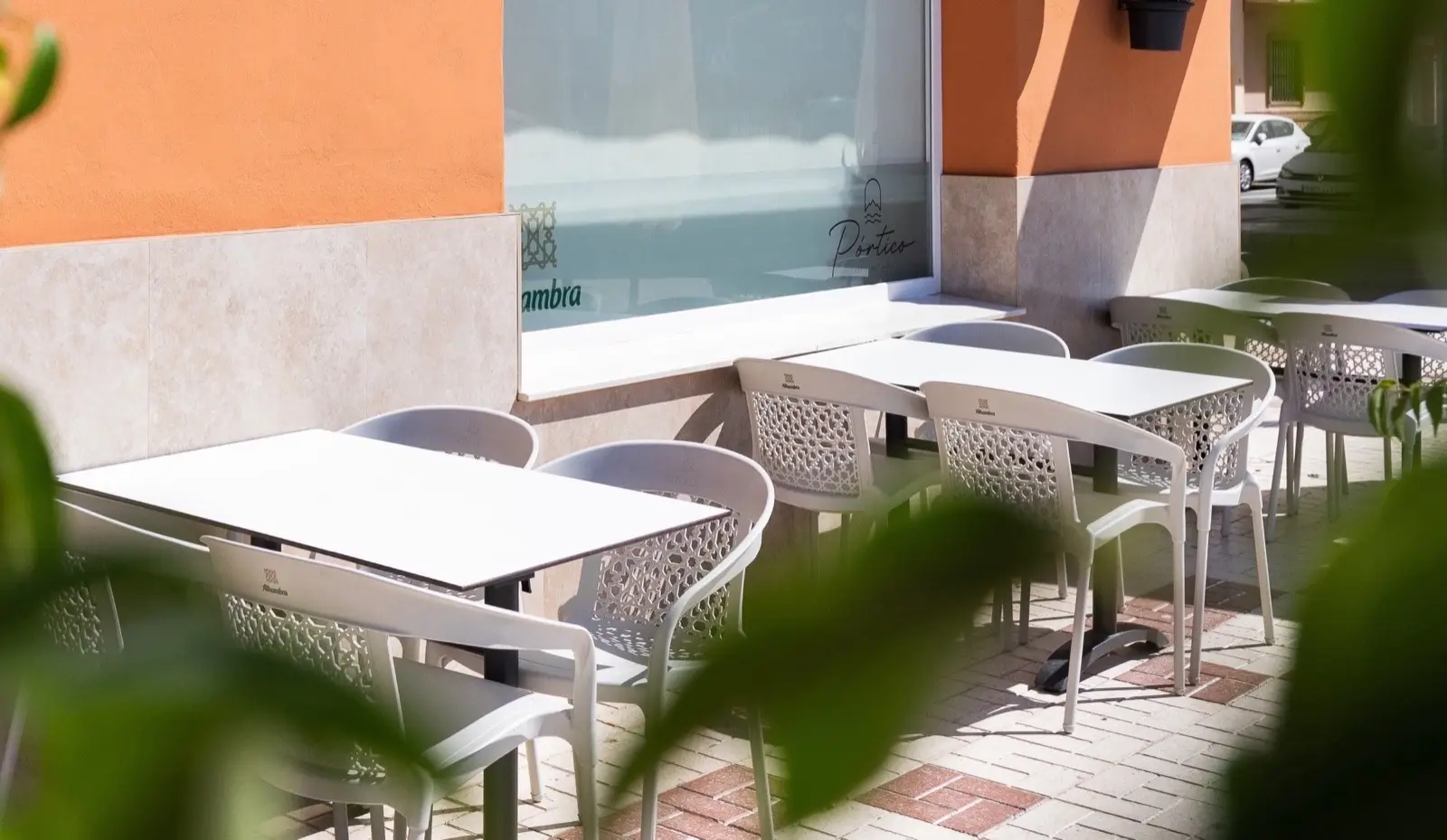 Terraza al aire libre con mesas blancas y sillas blancas de rejilla junto a la fachada naranja del restaurante.