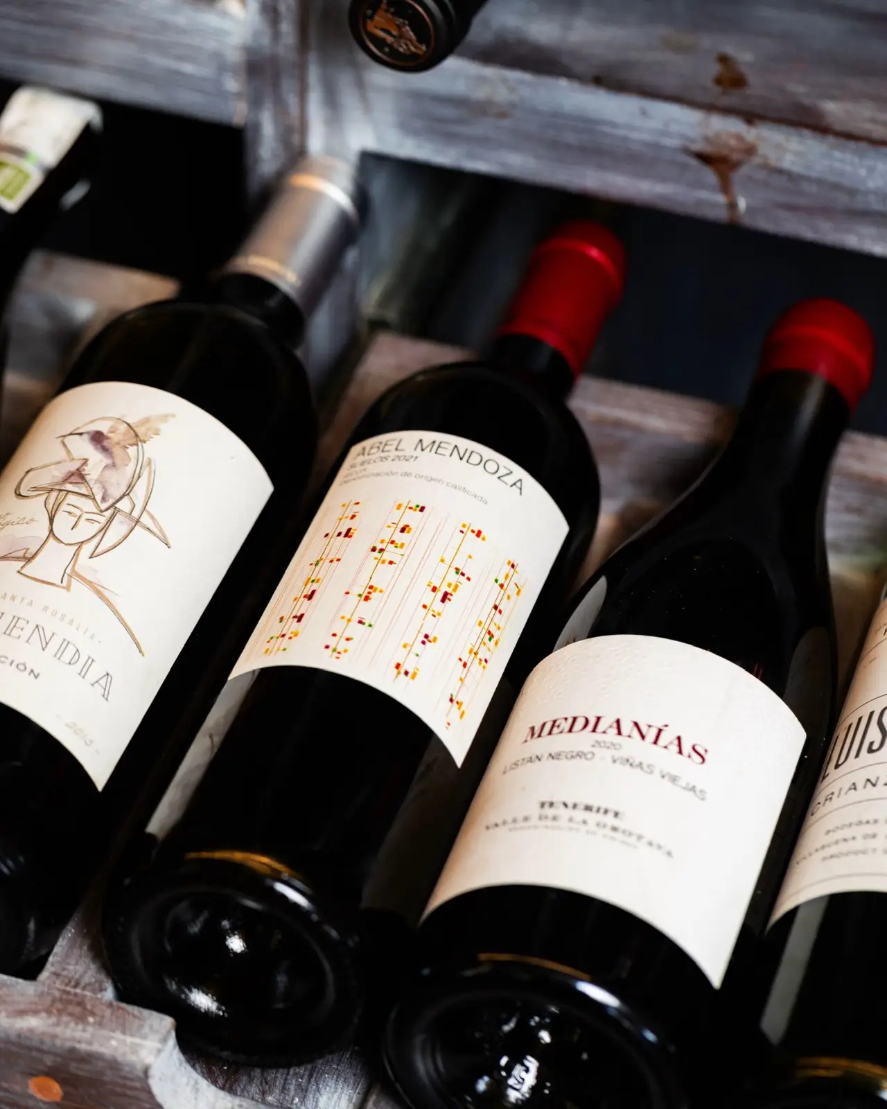 Botellas de vino tumbadas en un botellero de madera, con etiquetas de Mendoza y Medianías a la vista.